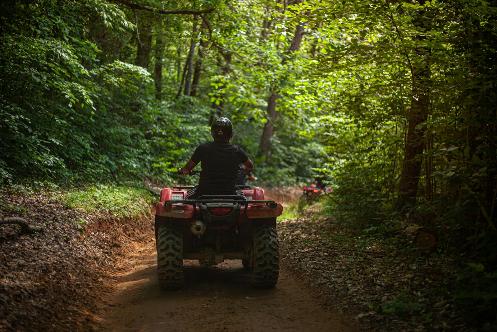 A person driving an ATV through a lush green forest trail, enjoying an adventurous ride.